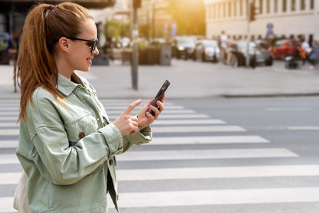 Modern urban woman uses a mobile phone while walking along a city street.の写真素材