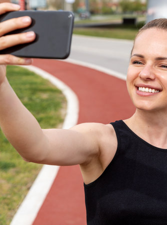 Athletic woman takes selfie while running on running track in city.の写真素材