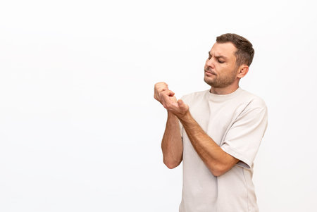 Adult man stands against white background and looking at his manicure.