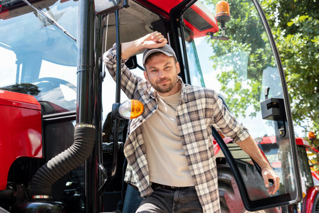 Portrait of man agriculture farmer posing next to his red tractor.