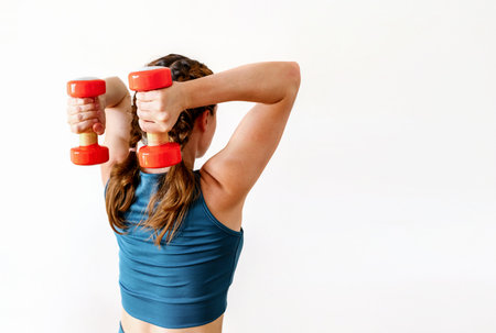 Rear view of female athlete doing triceps extension exercise with dumbbells, isolated on a white...