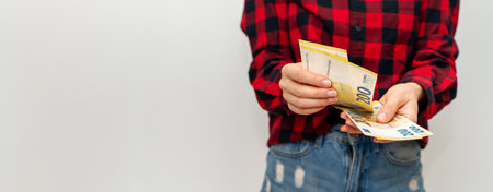Hands of a woman in a red checkered shirt with money on a white background