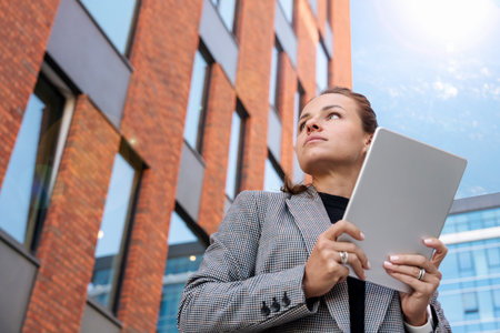 Confident businesswoman with tablet standing outside modern office building.