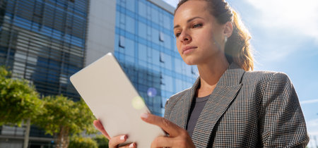 Businesswoman works on a digital tablet outside an office building. Digital innovation for e-commerce. Cybersecurity solution for e-banking. E-safety.の写真素材