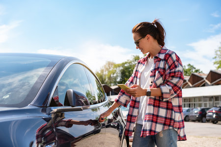 Urban woman unlocking parked car remotely using her smartphone. Car-sharing service. Automotive wireless technologies.の写真素材