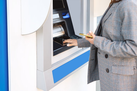 Businesswoman in a smart casual outfit using an ATM on a city street.の写真素材