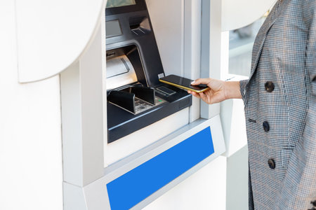 Person using smartphone for cash withdrawal at ATM.の写真素材