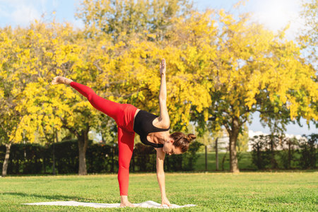 Fit woman practicing yoga on a sunny day in a city park.の写真素材