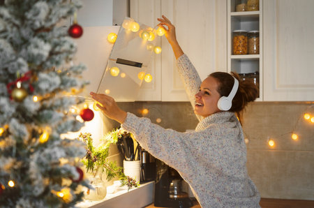 Cheerful woman in wireless headphones decorating her living room with a garland in preparation for Christmas.の写真素材