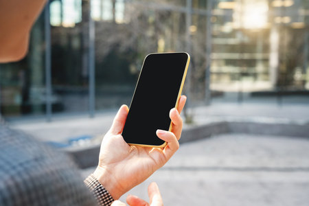 Smartphone with blank black screen in hand of businesswoman on city street.の写真素材