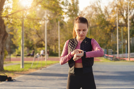Female athlete in sportswear using a smartwatch on an outdoor sports ground in city.