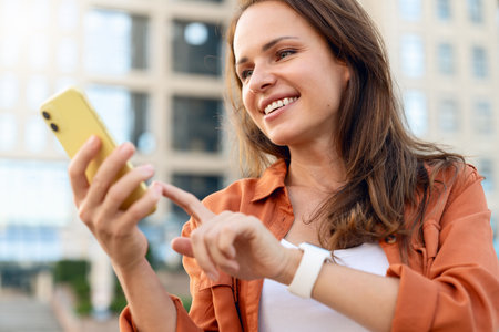 Brunette Caucasian woman wearing a brown shirt using her smartphone outdoors on a city street.の写真素材