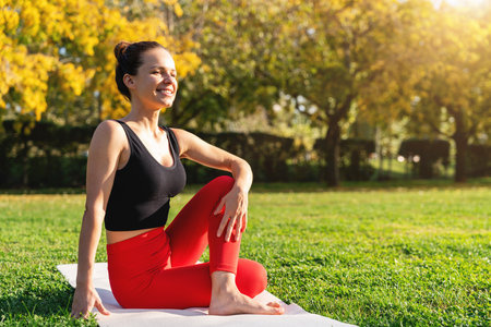 Fit woman practicing yoga outdoors on green grass in a city park.