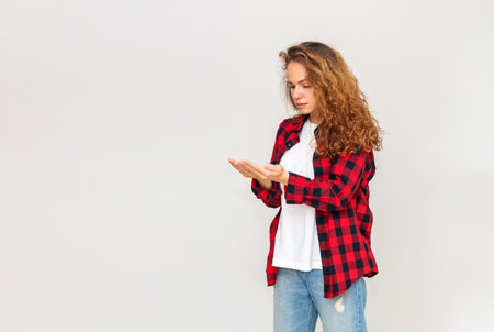 Isolated brunette curly-haired woman in a casual shirt looking at her palms in front of plain  light grey wall.の写真素材