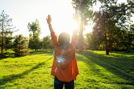 Rear view of woman with raised arms standing in front of greenery feeling free and happy while...