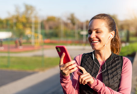 Smiling fit woman in earphones checking her smartphone during outdoor workoutの写真素材
