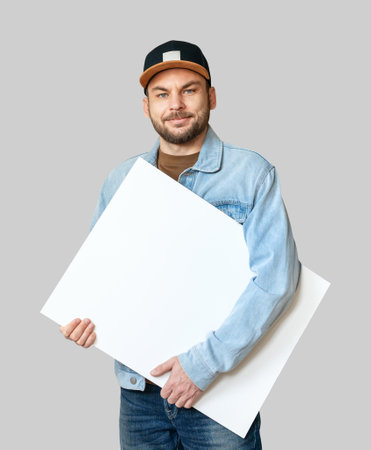 Cutout young adult man in denim jacket and snapback holding blank white canvas.の写真素材