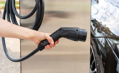 Woman's hand holding EV charging connector at EV station.の写真素材