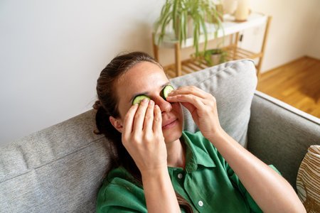 Woman applying cucumber slices on face at home for skincareの写真素材
