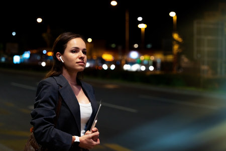 Modern businesswoman after work waiting for transport at night on city streetの写真素材