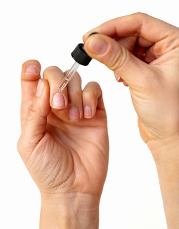 Close-up of female hand applying cuticle oil on natural nails using oil dropper.の写真素材