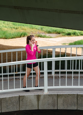 Active woman in pink t-shirt on footbridge preparing for outdoor summer workout