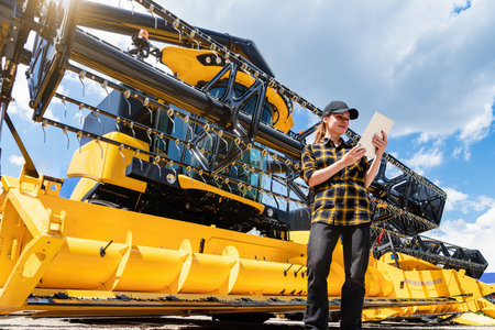 Young woman operating digital tablet near yellow combine harvester outdoorsの写真素材