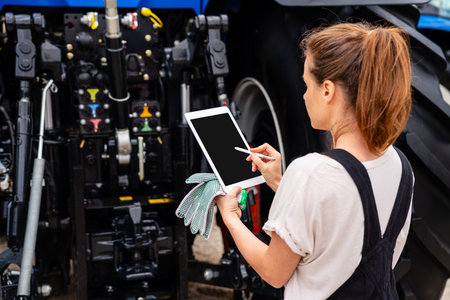 Female mechanic using digital tablet to manage farm equipment repairの写真素材
