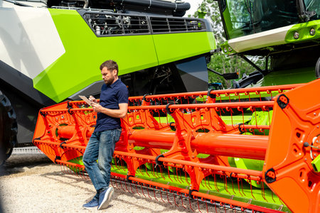 Agriculture industry worker using tablet by combine harvester at equipment dealershipの写真素材