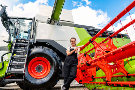Confident female farmer leaning on combine harvester outdoorsの写真素材
