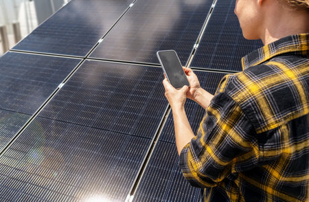 Female maintenance worker checking solar panel performance on smartphoneの写真素材