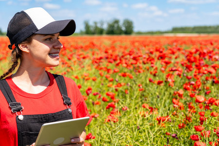 Smiling young woman with tablet by scenic red poppy field outdoors. Environmental restoration.