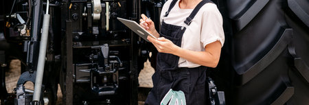 Woman technician inspecting tractor with digital tablet at farm equipment site