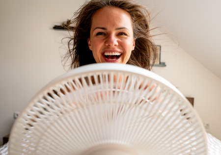 Laughing woman cooling down in front of fan with wind blowing through her hairの写真素材