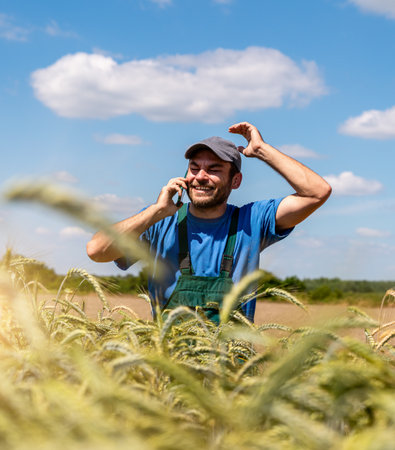 Cheerful male farmer deeply engaged in lively phone conversation near cereal field