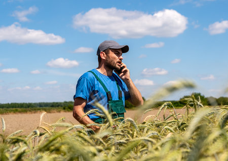 Farmer in cap talking on phone by cereal field about harvest planning