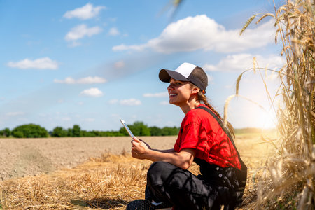 Female agricultural worker using digital tablet while sitting on farmland near field
