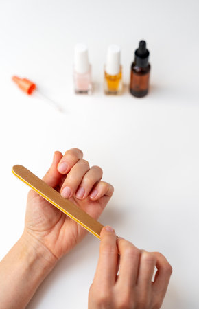 Close-up of female hands filing nails with nail file on white deskの写真素材