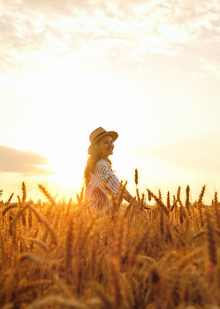 Happy woman enjoying sunset in agricultural cereal field in summerの写真素材