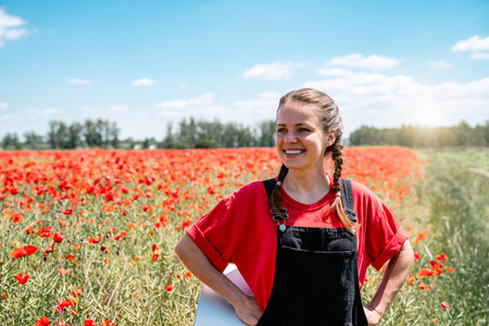 Happy young woman standing in blooming red poppy field promoting nature restoration and biodiversityの写真素材
