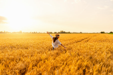 Happy woman with arms wide open enjoying freedom in summer grain field at sunsetの写真素材