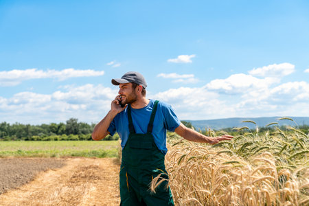 Agricultural worker speaking on smartphone near cereal crops.
