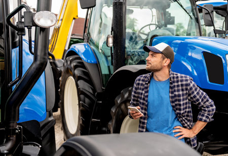 Male buyer holding phone and inspecting tractors at farming dealership