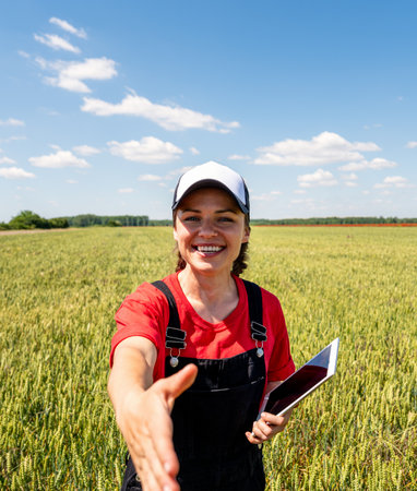 Smiling female farmer extending hand for handshake in green wheat field, POV perspective.