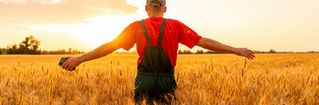 Back view of farmer with open arms embracing rural life in wheat field golden sunset