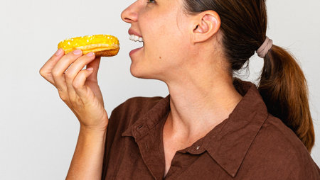 Profile portrait cheerful female eating donut with yellow glaze