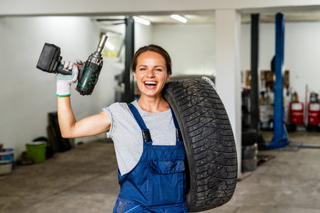 Portrait of a cheerful female tire fitter at work. Woman holding vehicle tire and impact wrench.の写真素材