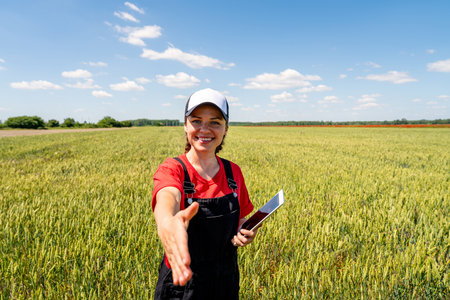 Female farmer with digital tablet in wheat field reaching hand for handshake