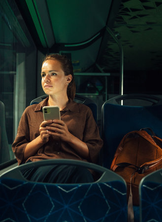 Woman commuter holding smartphone while riding night busの写真素材