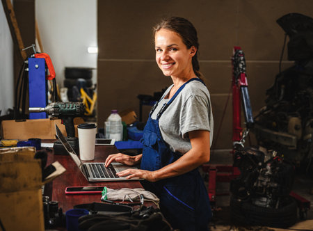 Female auto mechanic working on laptop in local car repair shop.の写真素材
